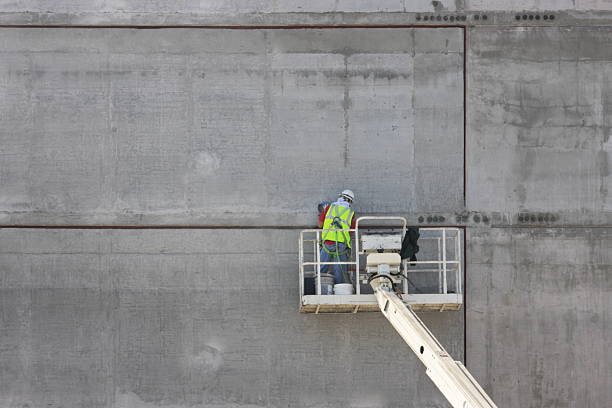 A worker on a lift performing commercial concrete wall maintenance in Pearson, GA, showcasing safety and precision in a construction environment.