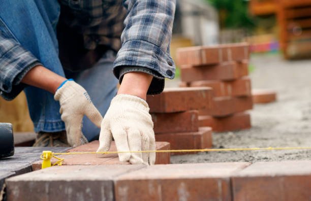 Driveway installation contractor laying bricks on a pathway, carefully arranging each piece for a sturdy and even surface.