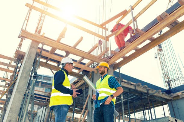 Two local concrete contractors in Dallas, GA engaged in conversation on a busy construction site, surrounded by equipment and building materials.