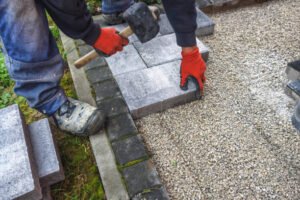 A man uses a hammer to secure cement blocks during a commercial driveway installation on a busy sidewalk area.