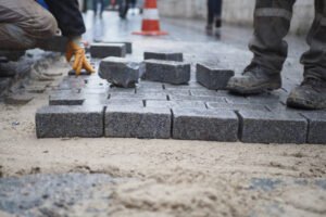 A man laying bricks on a sidewalk, carefully arranging them in a neat pattern as part of a commercial driveway installation.