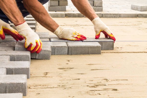 A man laying bricks on a sidewalk, carefully arranging them in a neat pattern as part of a commercial driveway installation project.