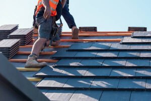 Two men installing roofing shingles on a sloped concrete roof, focused on their work and using safety equipment. 
