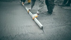 A man working on a sidewalk by pouring concrete, highlighting concrete services available in Mableton, GA.