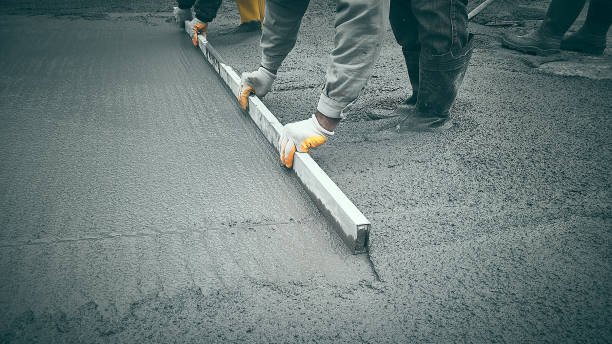 Professional contractors leveling a fresh cement surface before applying decorative stamped concrete patterns.
