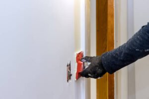  A person carefully cutting white plaster with a knife, showcasing a drywall repair process.