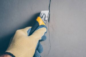  Individual removing plaster from a wall with a tool, showcasing drywall repair work in progress. doing work Drywall Repair Near Me