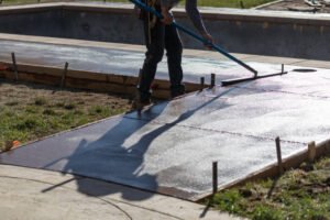A man uses a hose to wash concrete, highlighting his role as a contractor specializing in driveways, patios, and foundations.