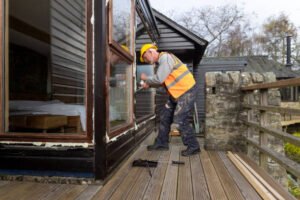 A man wearing an orange safety vest is engaged in building a wooden deck for a patio.