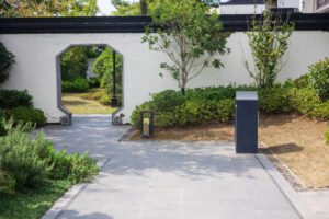 A white gate beside a black gate and a black box, set against a backdrop of newly installed concrete patio.