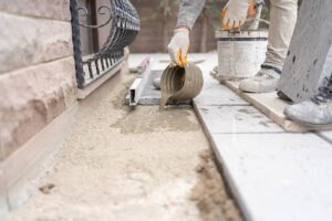 A man pouring concrete onto a sidewalk during a patio installation project.