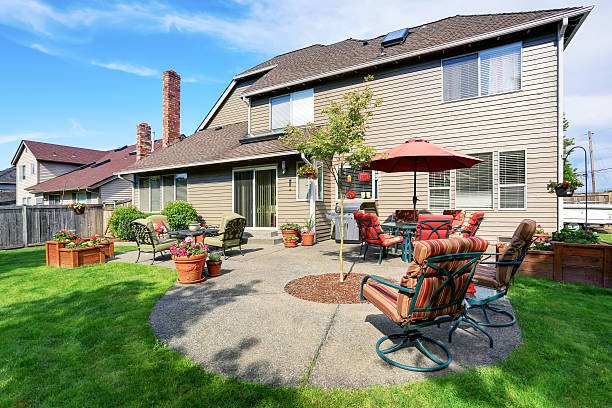 A yard with a concrete patio, equipped with chairs and a colorful umbrella for shade.