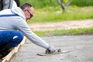 A man is working on a concrete slab, preparing it for a stamped concrete driveway installation.