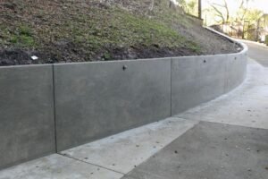 Concrete retaining wall positioned in front of a house, providing support and landscaping features to the property.