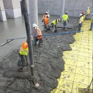 Construction workers pouring and leveling fresh wet Commercial Concrete on a large job site